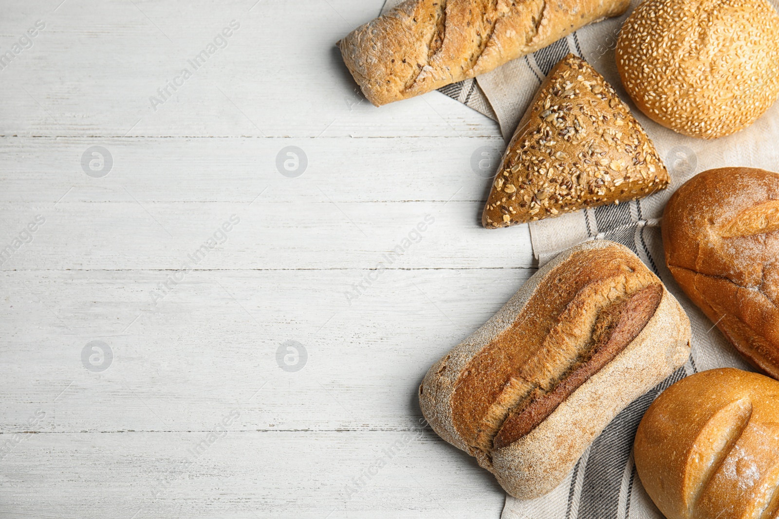 Photo of Loaves of different breads on white wooden background, flat lay. Space for text