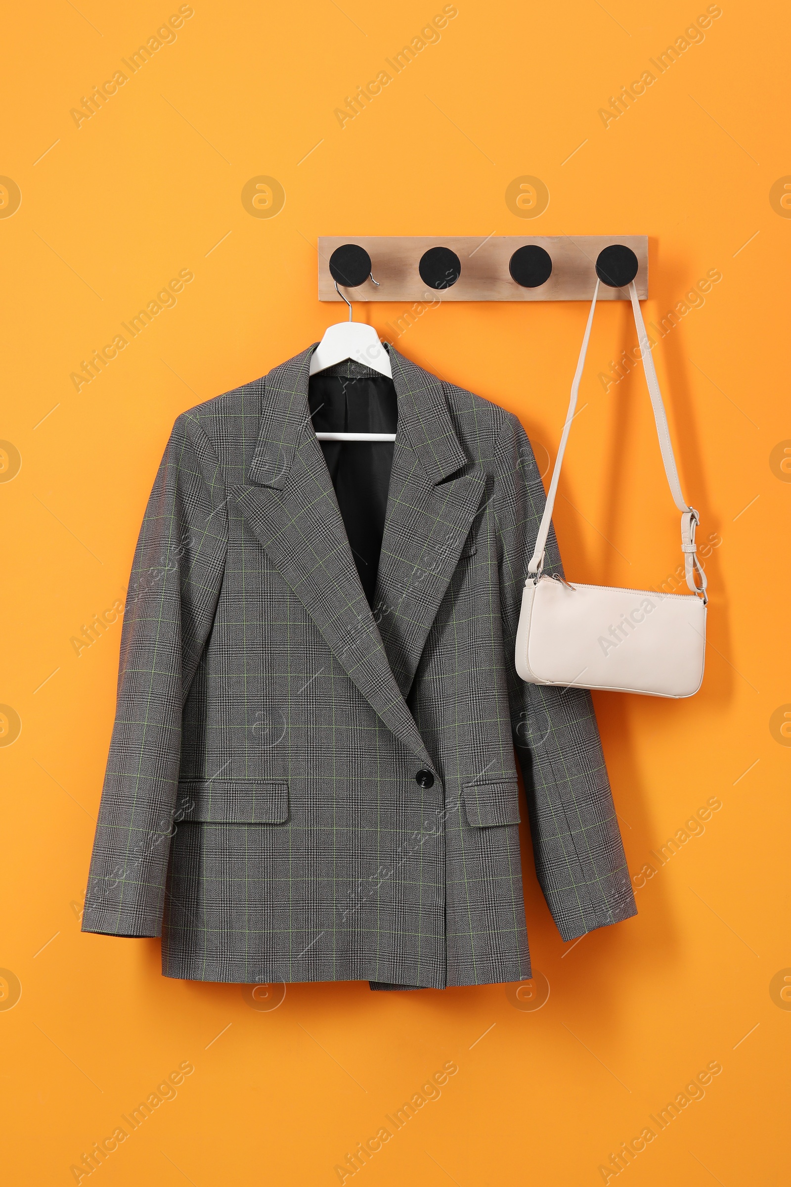 Photo of Hanger with stylish jacket and bag on orange wall