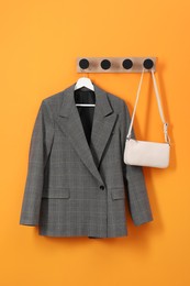 Photo of Hanger with stylish jacket and bag on orange wall