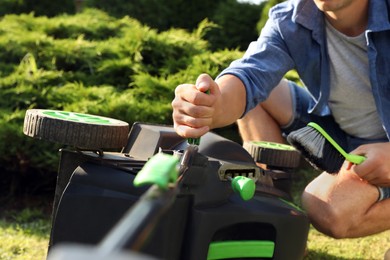 Photo of Young man fixing lawn mower in garden, closeup