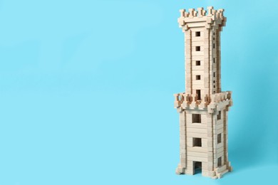 Photo of Wooden tower on light blue background, space for text. Children's toy