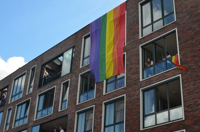 Photo of AMSTERDAM, NETHERLANDS - AUGUST 06, 2022: Building facade with bright LGBT pride flags and people looking out of windows at parade