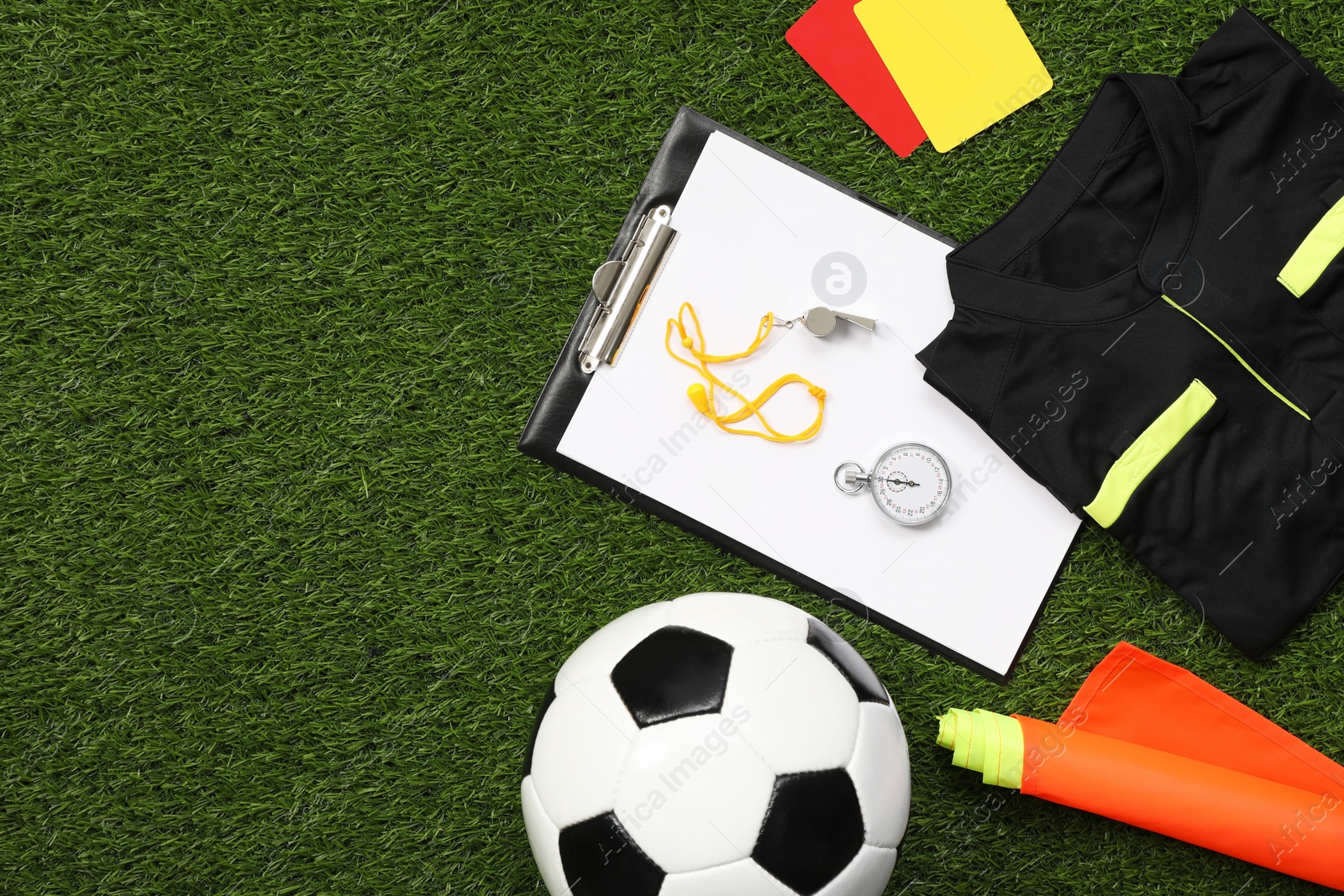 Photo of Uniform, soccer ball and other referee equipment on green grass, flat lay. Space for text