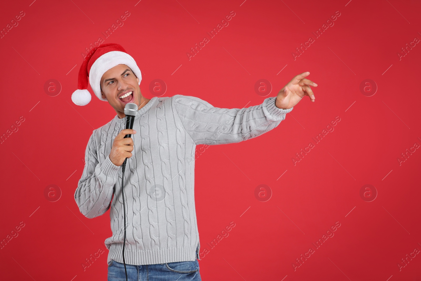 Photo of Happy man in Santa Claus hat singing with microphone on red background. Christmas music