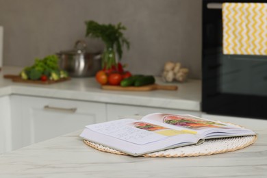 Recipe book on white marble table in kitchen, closeup. Space for text