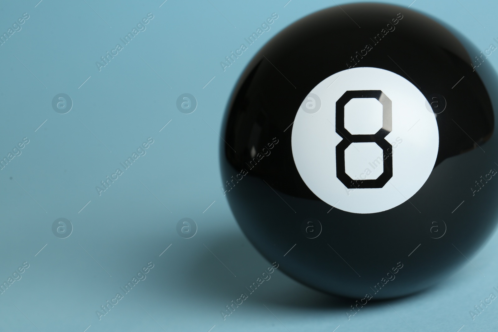 Photo of One magic eight ball on light blue background, closeup. Space for text