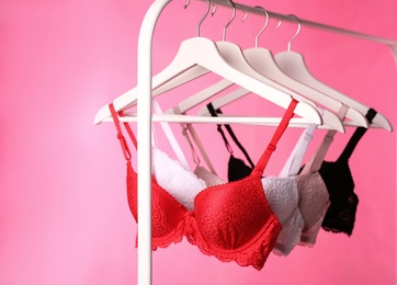 Hangers with beautiful lace bras on rack against pink background. Stylish underwear