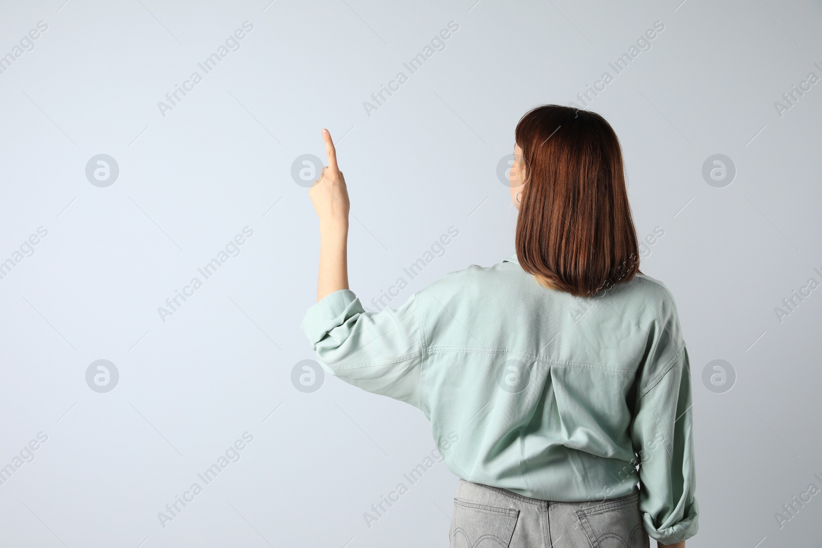Photo of Young girl pointing on white background, back view. Space for text