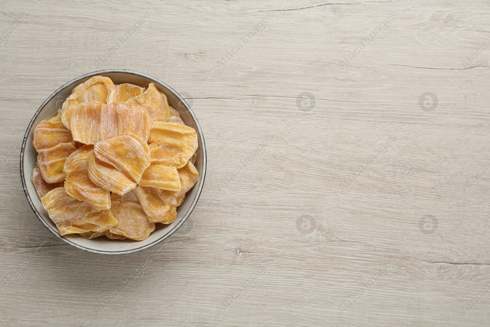 Photo of Delicious dried jackfruit slices in bowl on light wooden table, top view. Space for text