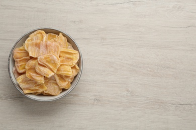 Delicious dried jackfruit slices in bowl on light wooden table, top view. Space for text