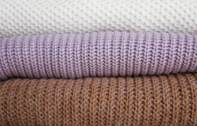 Photo of Stack of folded knitted sweaters as background, closeup