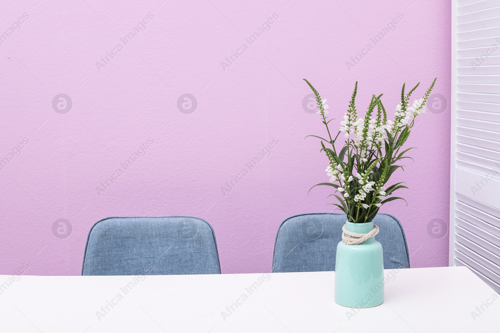 Photo of Beautiful bouquet in vase on white table against color background. Stylish interior