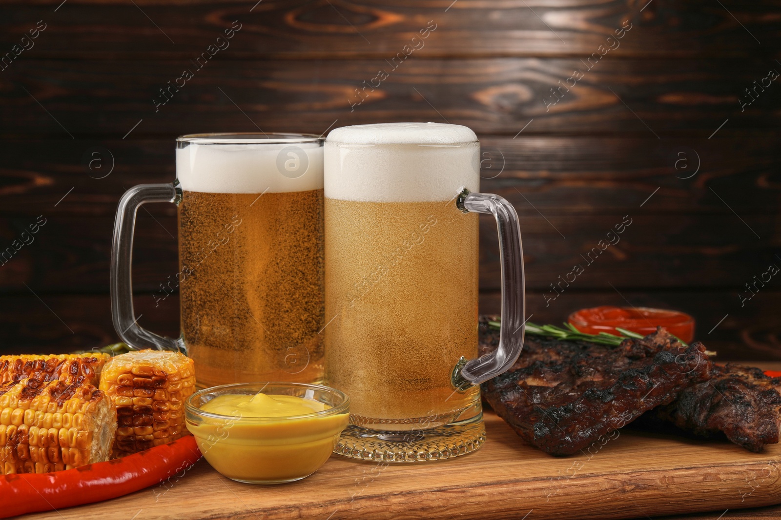 Photo of Mugs with beer, delicious grilled ribs and ingredients on wooden table