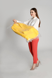 Young woman holding hanger with jacket on light grey background. Dry-cleaning service