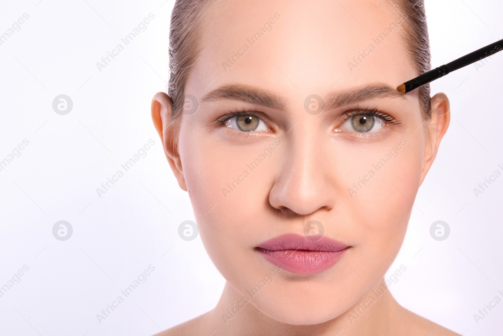 Photo of Beautiful woman with perfect eyebrows applying makeup on light background