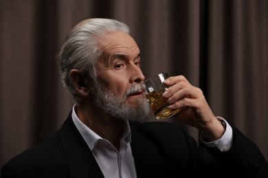 Senior man in suit drinking whiskey on brown background