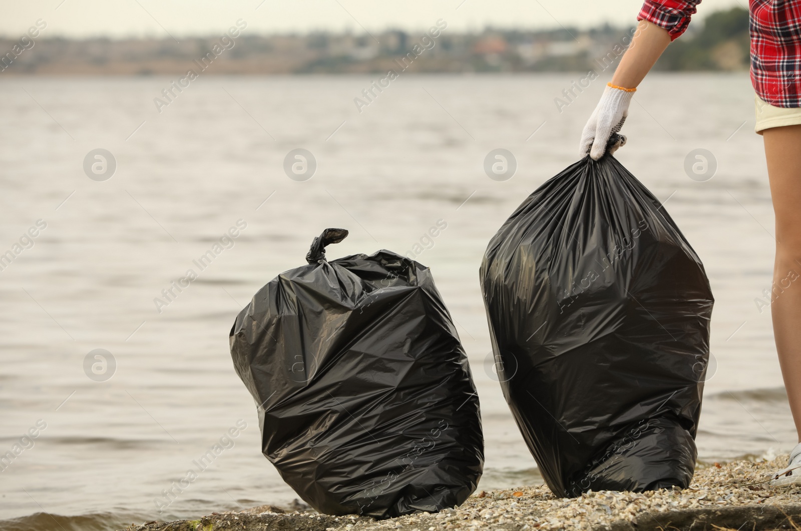 Photo of Woman with trash bags full of garbage on beach, closeup