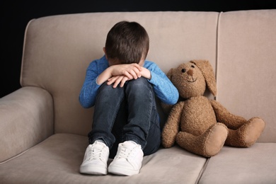 Sad little boy with toy sitting on couch at home