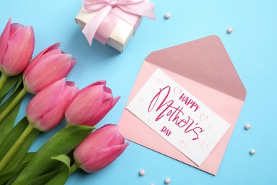 Happy Mother's Day greeting card, envelope, beautiful tulip flowers and gift box on light blue background, flat lay