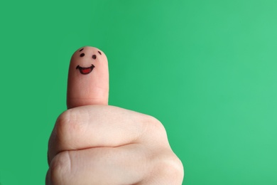 Photo of Finger with happy face drawing on green background. Space for text