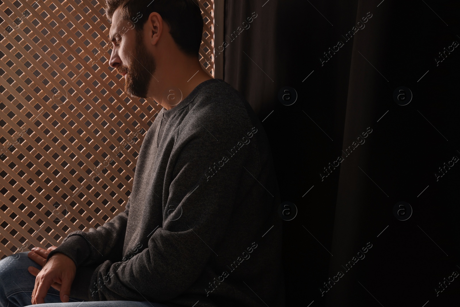Photo of Upset man listening to priest during confession in booth