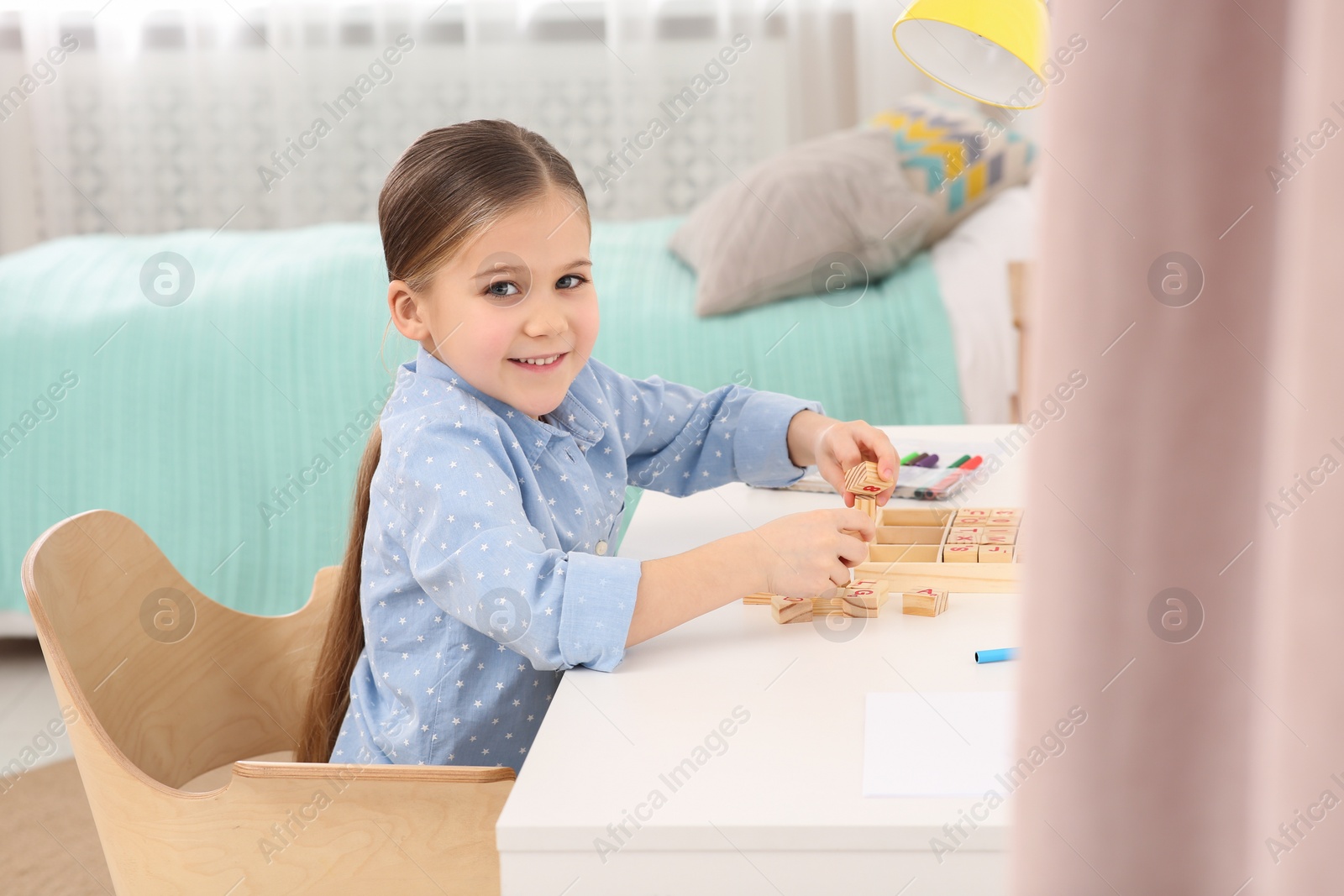 Photo of Cute little girl playing with wooden cubes at desk in room. Home workplace