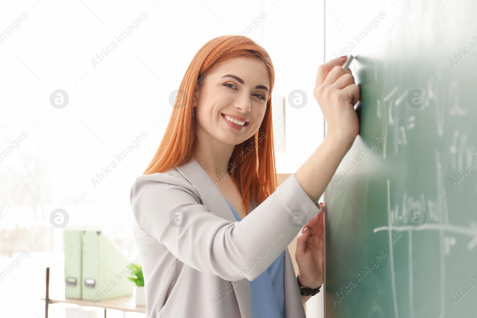 Photo of Beautiful young teacher writing on blackboard in classroom