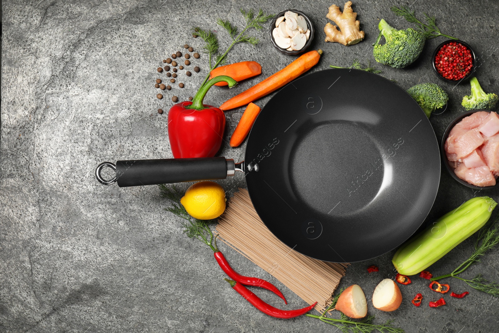 Photo of Empty iron wok surrounded by raw ingredients on grey table, flat lay