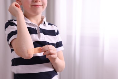 Photo of Little boy putting sticking plaster onto elbow indoors, closeup. Space for text