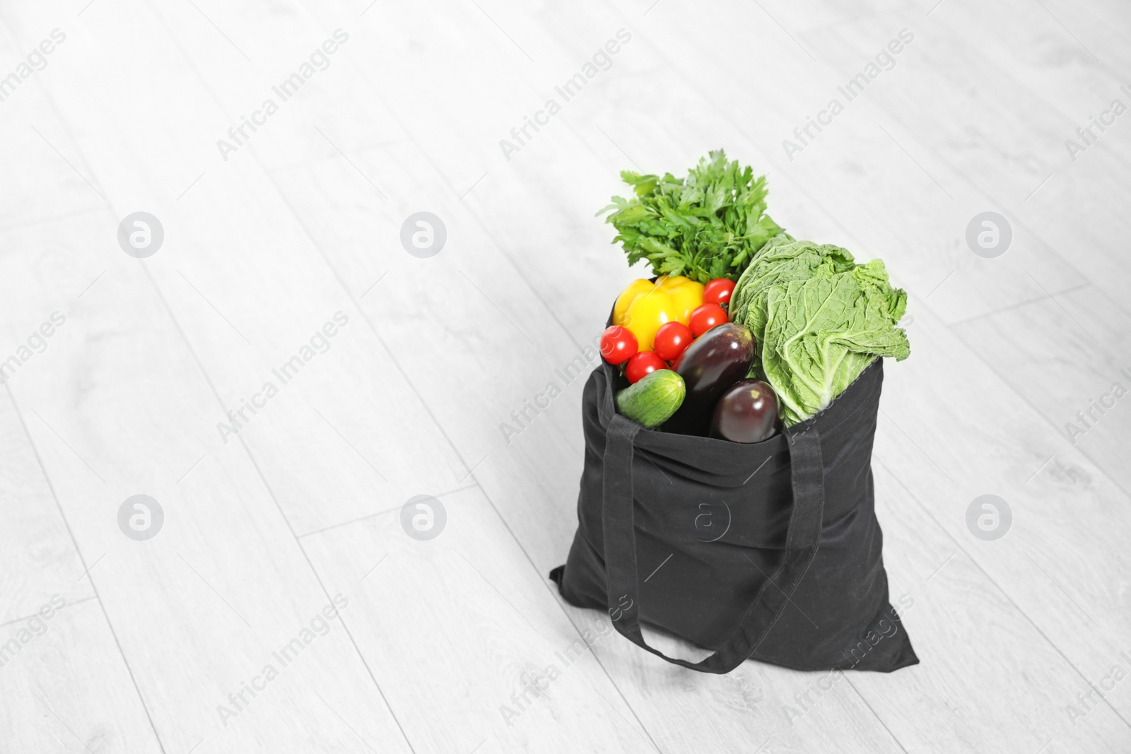 Photo of Textile shopping bag full of vegetables on floor. Space for text