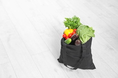 Photo of Textile shopping bag full of vegetables on floor. Space for text