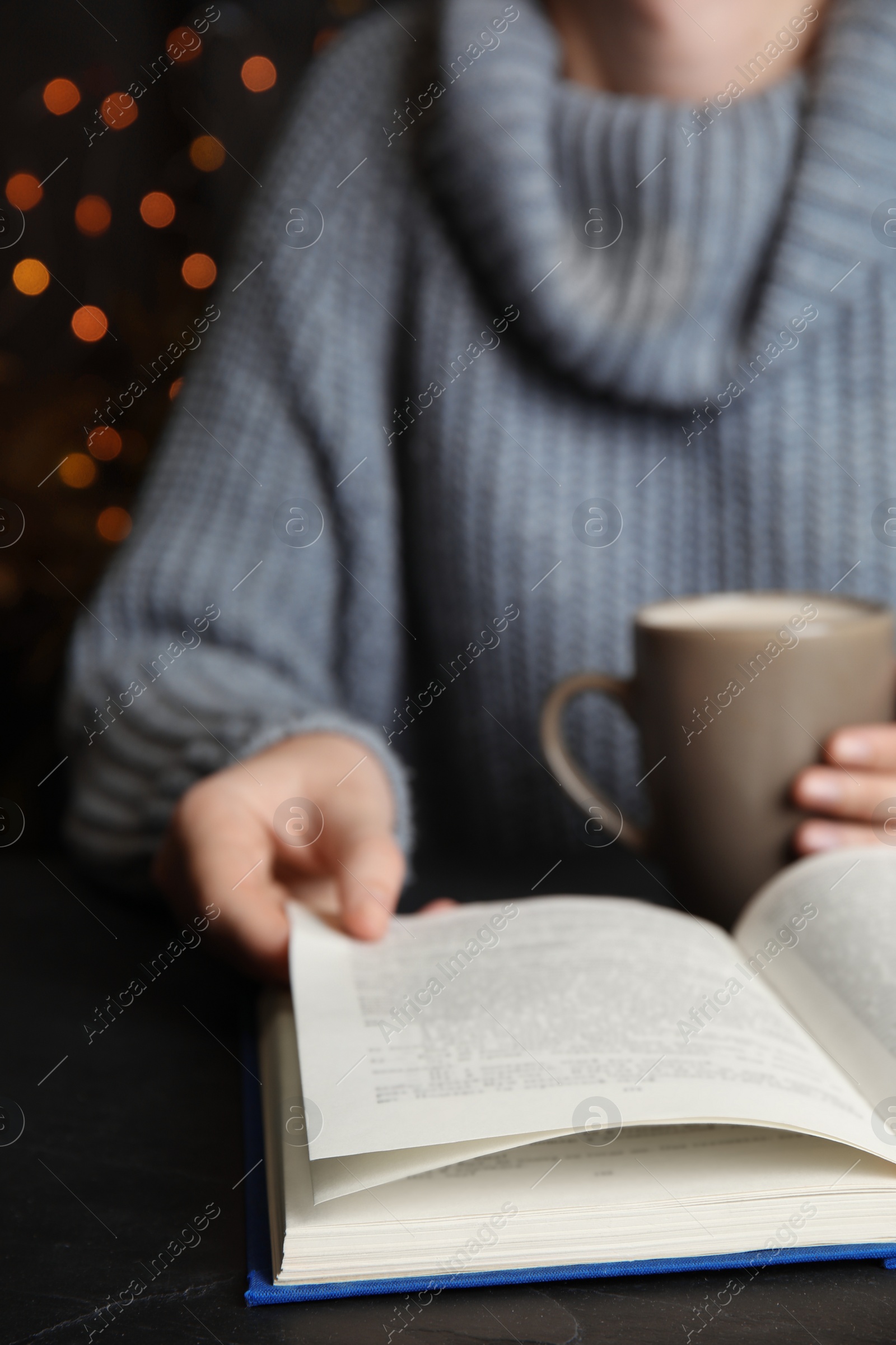 Photo of Woman with cup of coffee reading book at table, closeup