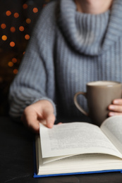 Photo of Woman with cup of coffee reading book at table, closeup