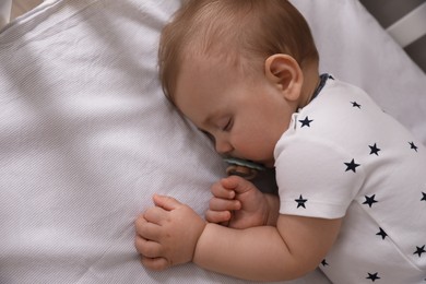 Adorable little baby with pacifier sleeping in crib, above view