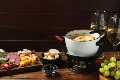 Photo of Fork with piece of sausage, melted cheese in fondue pot and other products on wooden table. Space for text