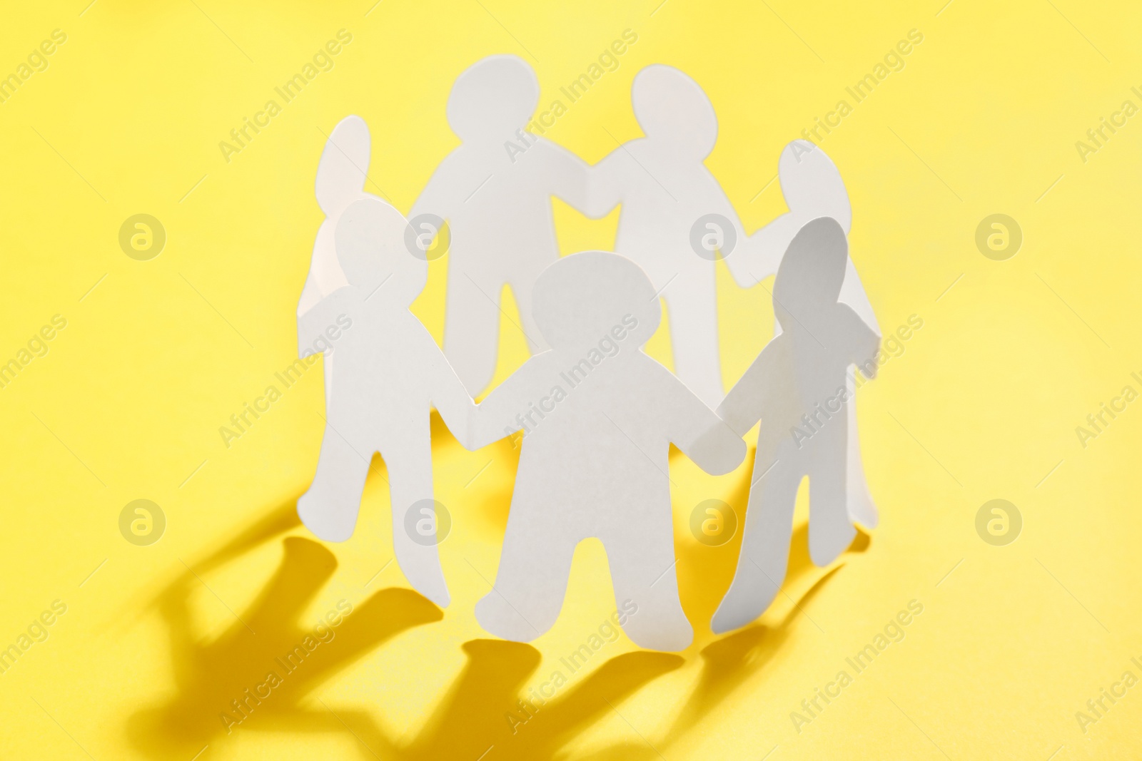 Photo of Paper people chain making circle on yellow background. Unity concept