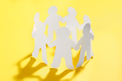 Photo of Paper people chain making circle on yellow background. Unity concept