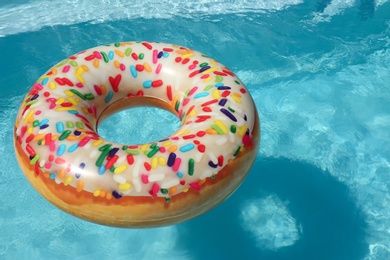 Bright inflatable doughnut ring floating in swimming pool on sunny day