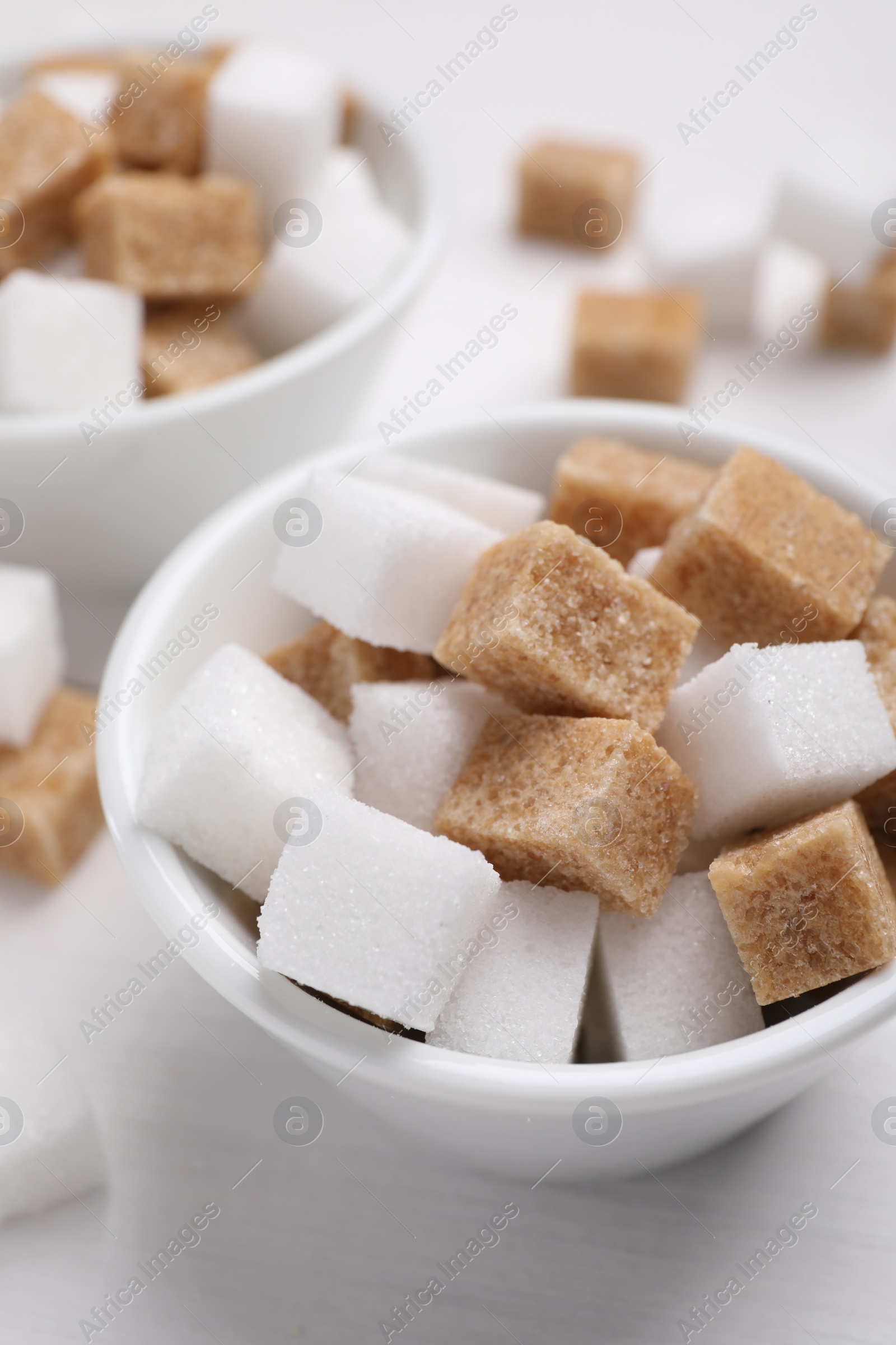 Photo of Different sugar cubes in bowl on white table, closeup