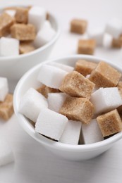 Different sugar cubes in bowl on white table, closeup