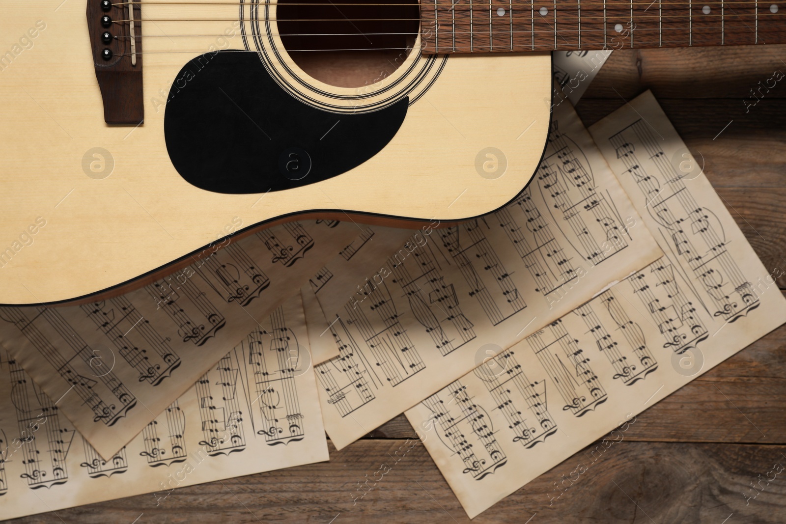 Photo of Paper sheets with music notes and acoustic guitar on wooden table, top view