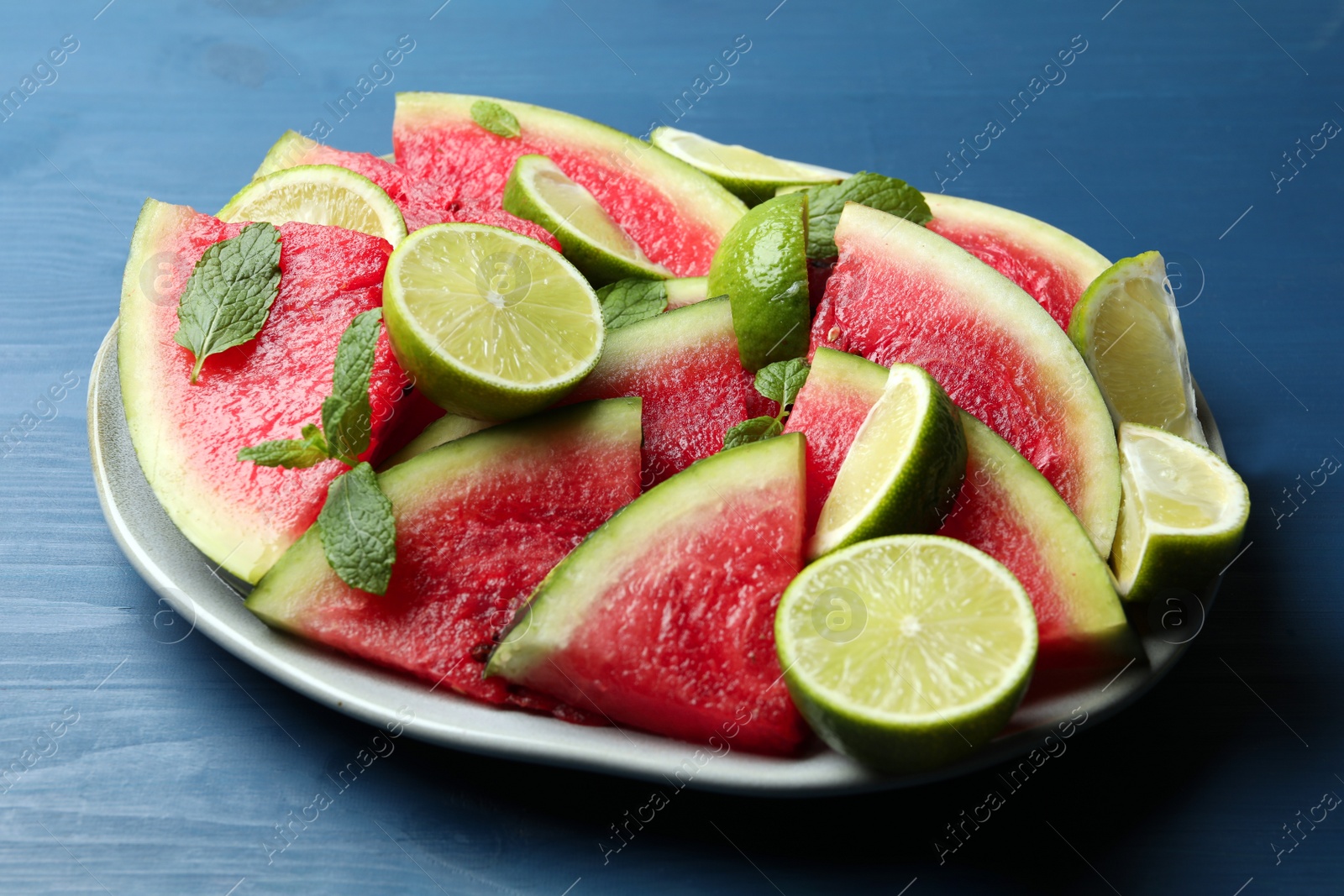 Photo of Plate with cut juicy watermelon and lime on blue wooden table