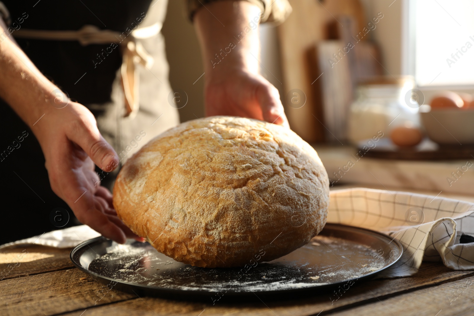 Photo of Man holding loaf of fresh bread at wooden table indoors, closeup