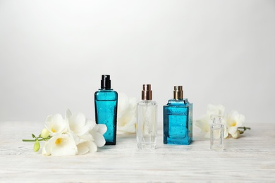 Bottles of perfume and flowers on table against light background