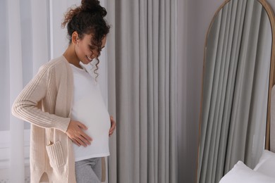 Photo of Pregnant young African-American woman near mirror at home