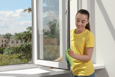 Photo of Happy young woman cleaning window with rag indoors
