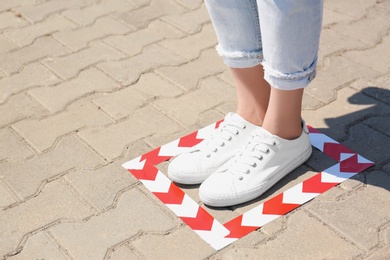 Photo of Woman standing on taped floor marking for social distance outdoors, closeup with space for text. Coronavirus pandemic