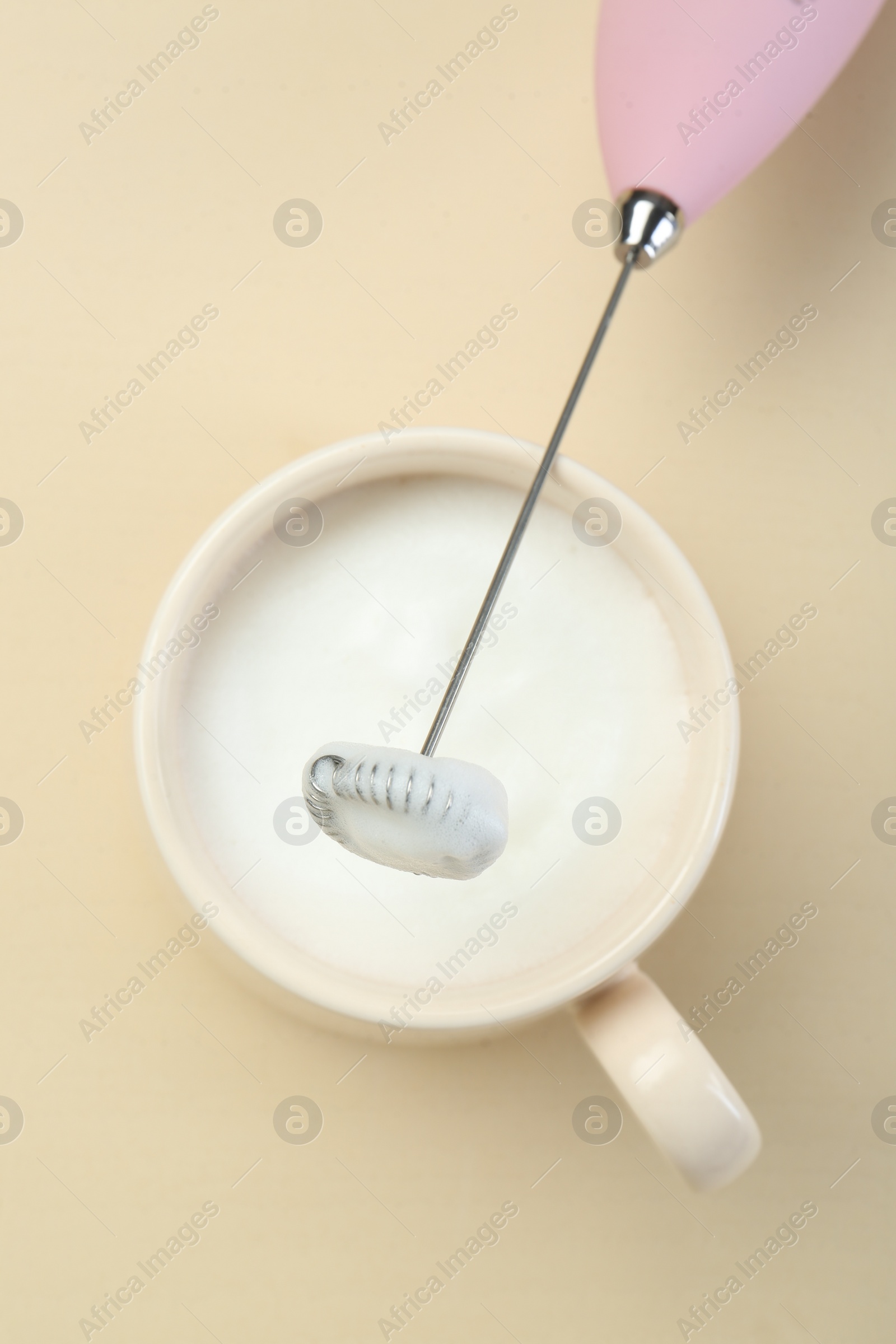 Photo of Mini mixer (milk frother) and cup of whipped milk on beige background, top view