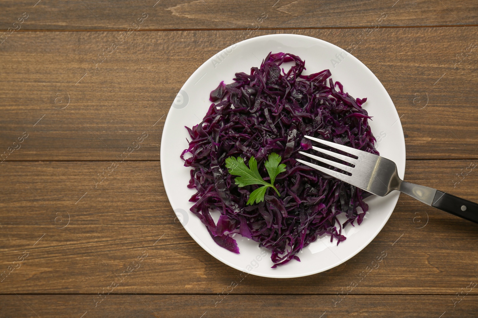 Photo of Tasty red cabbage sauerkraut with parsley on wooden table, top view. Space for text