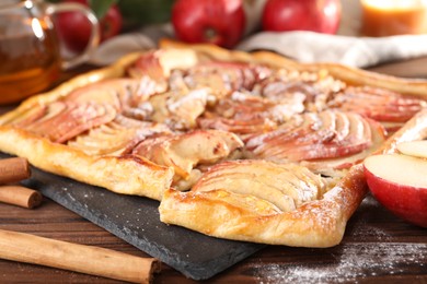 Photo of Tasty apple pie with powdered sugar, cinnamon sticks and fresh fruit on wooden table, closeup